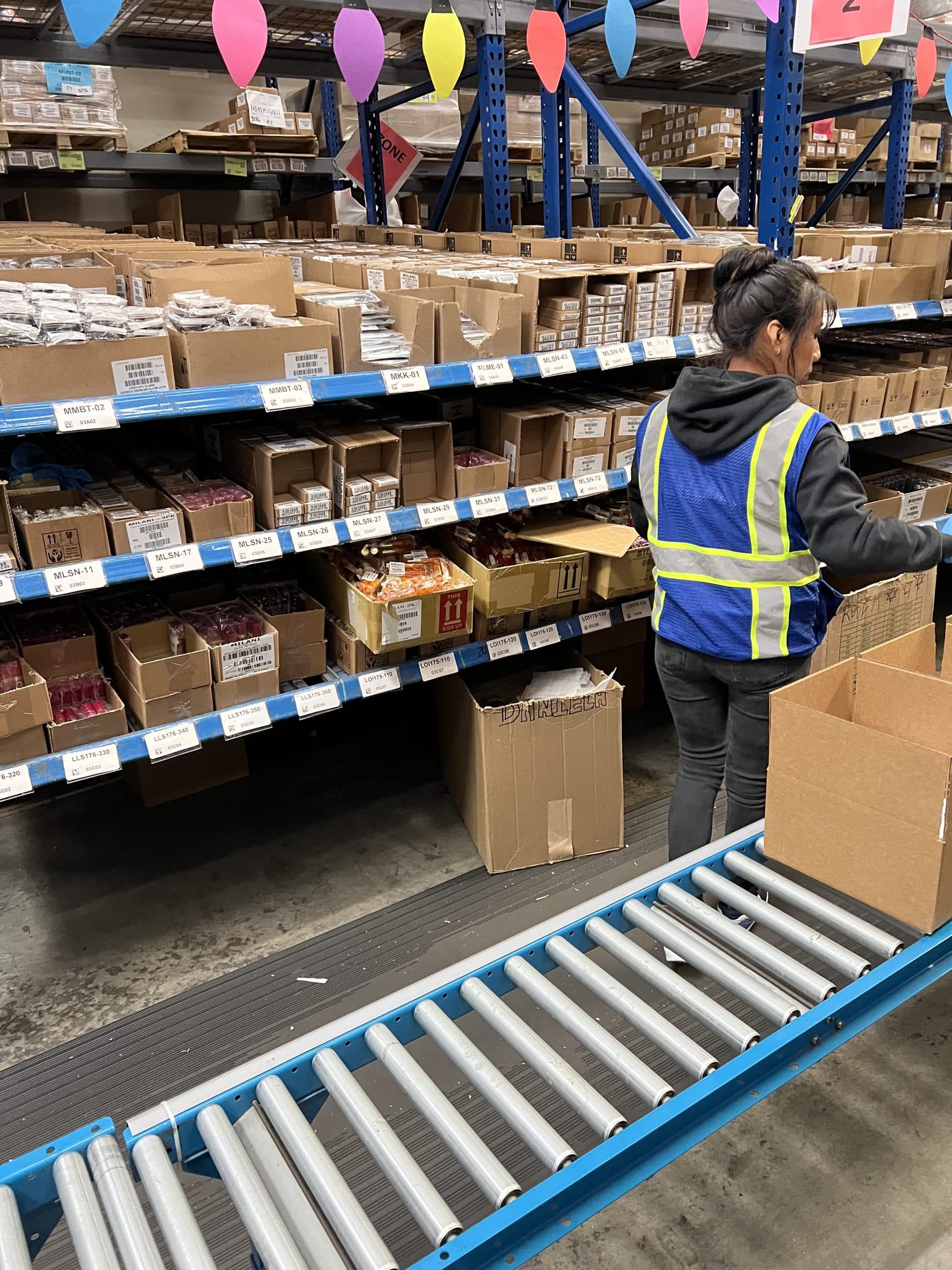 A picker working a shelving line beside a roller conveyor